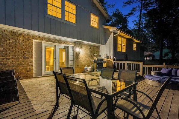 A deck with a glass-top table and chairs, a barbecue grill, and a covered area with a bench.