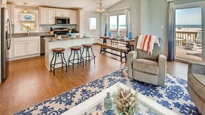 A spacious kitchen with white cabinets, a central island, and a dining area with a view of the beach. - Oceanfront Dog Friendly Home with Home Theater, Hot Tub, Grill (Waves)