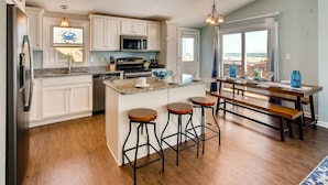 A modern kitchen with white cabinets, a granite countertop, and a central island with stools. - Oceanfront Dog Friendly Home with Home Theater, Hot Tub, Grill (Waves)