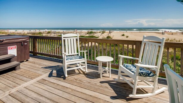 A wooden deck with two rocking chairs and a small table, overlooking a beach with sand dunes and the ocean. - Oceanfront Dog Friendly Home with Home Theater, Hot Tub, Grill (Waves)