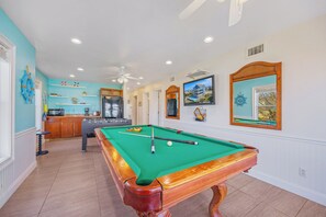 A pool table in a room with a kitchen area, a ceiling fan, and a television mounted on the wall. - Oceanview Dog Friendly Home w/ Private Pool, Hot Tub, Elevator, and Game Room (Rodanthe)