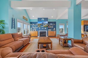 A spacious living room with a fireplace, a dining area, and a kitchen with wooden cabinets. - Oceanview Dog Friendly Home w/ Private Pool, Hot Tub, Elevator, and Game Room (Rodanthe)