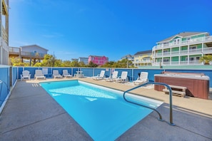 A swimming pool with lounge chairs and a hot tub, surrounded by a blue fence and buildings in the background. - Oceanview Dog Friendly Home w/ Private Pool, Hot Tub, Elevator, and Game Room (Rodanthe)