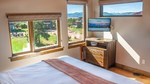 Un dormitorio con cama, cómoda de madera, televisor y ventanas amplias con vistas a la montaña.