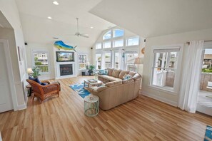 A spacious living room with a fireplace, a large sofa, and a ceiling fan. - Oceanview Down By The Sea! Home w/ Pool, Hot Tub, Elevator, Pier Passes, Game Rm (Rodanthe)