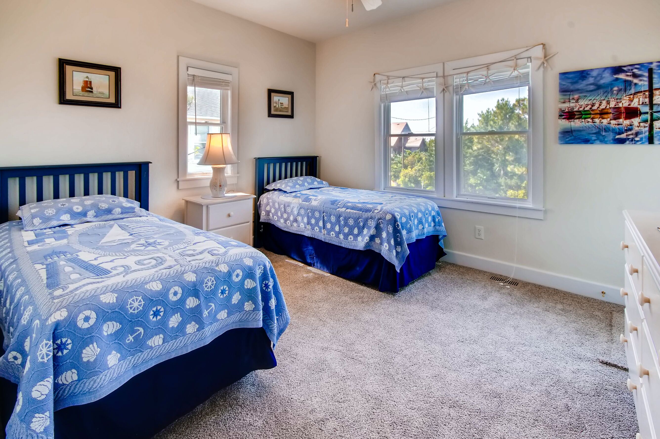 A bedroom with two beds, a nightstand, a window with a view, and a painting on the wall.