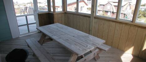 Ett trädäck med ett picknickbord, stora fönster och utsikt över byggnader.