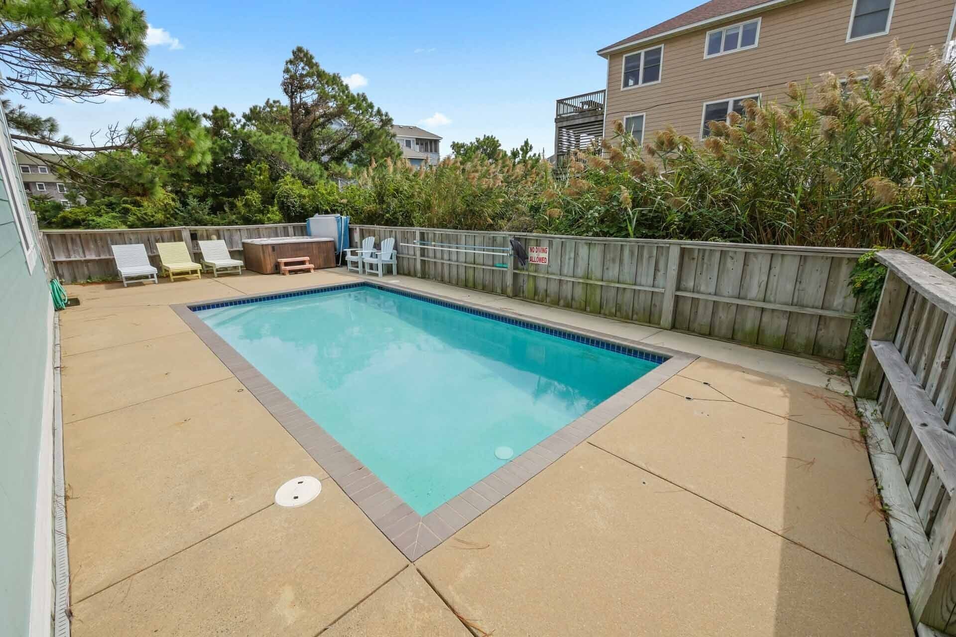 Piscina rectangular con muelle de madera, rodeada por una valla de madera y árboles.