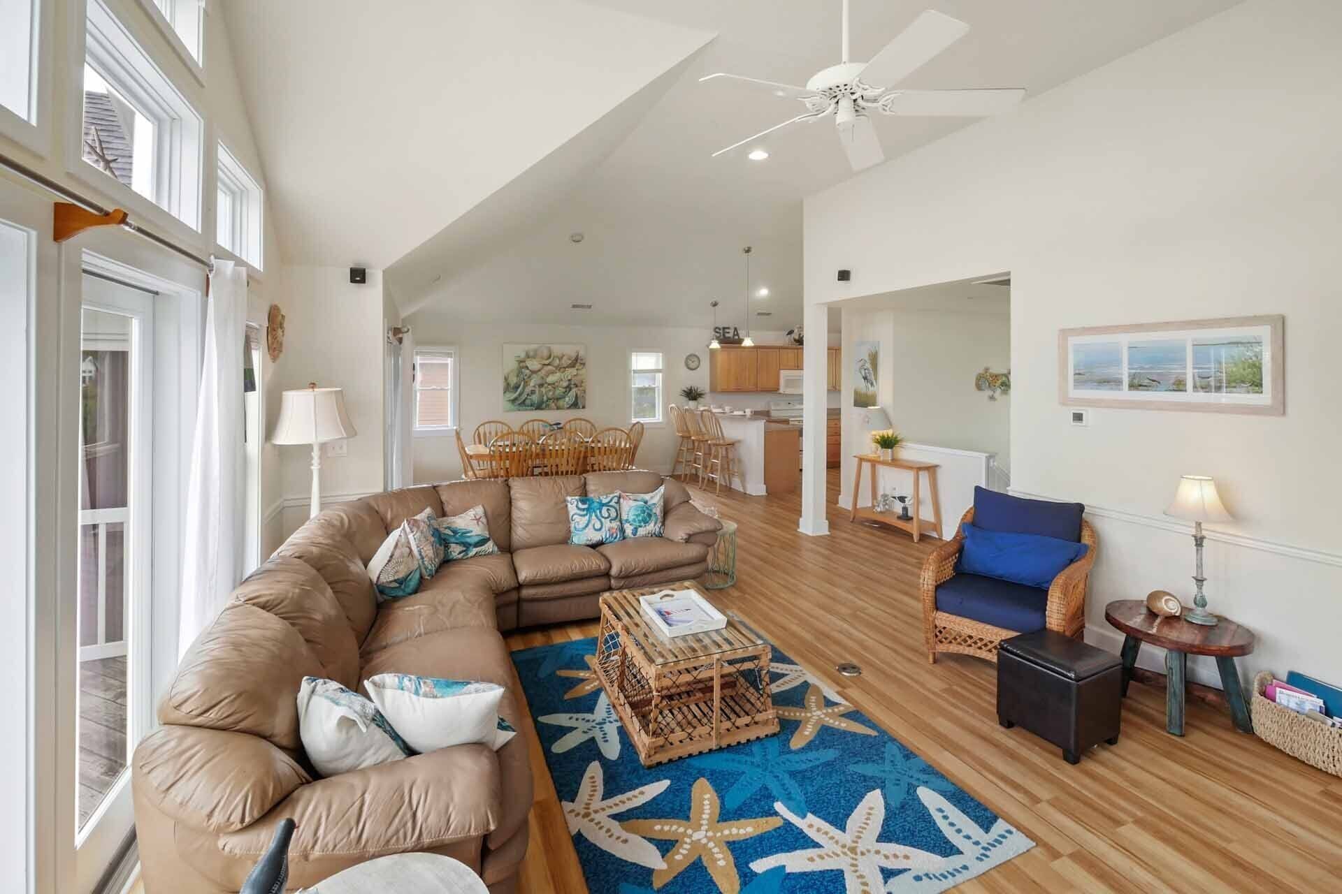 A spacious living room with a large brown sectional sofa, a blue starfish-patterned rug, and a ceiling fan.
