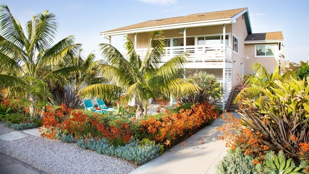 Une maison située en bord de mer, dotée d’un balcon, entourée de plantes tropicales et agrémentée d’une piscine.
