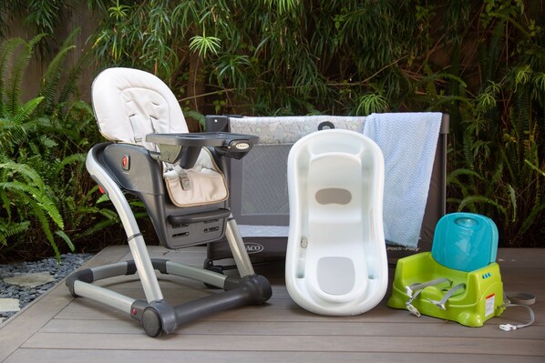 Um carrinho de bebê, um assento para bebê e um potty infantil em um deck de madeira, com samambaias ao fundo.