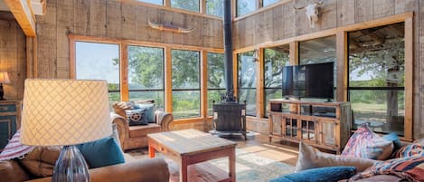 A spacious living room with a fireplace, comfortable seating, and large windows offering a view of the outdoors.