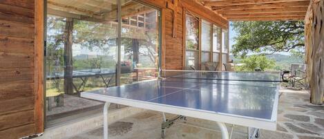 A ping pong table in a covered outdoor area with stone flooring and wooden walls.