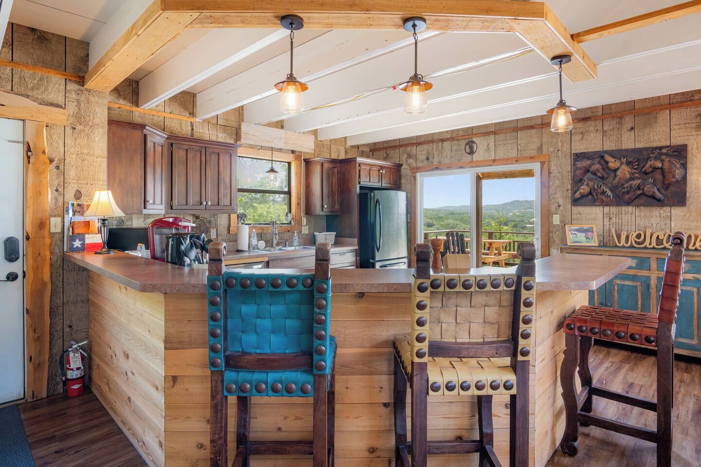A rustic kitchen with wooden walls and a bar area featuring stools with rivets.