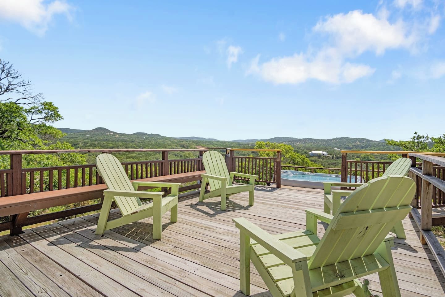 A wooden deck with green Adirondack chairs and a pool.