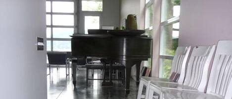 A hallway with a piano, white chairs, and patterned flooring.