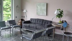 Ein modernes Wohnzimmer mit einem grauen Ecksofa, Stühlen mit Metallgestell, einem kleinen Tisch und einer Lampe.