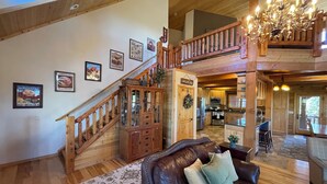 A spacious living area with a leather sofa, a staircase, and a kitchen in the background. - Sugar Knoll Lodge / 3 Story, 5bdr, HOT TUB, East Zion, Bryce and Grand Canyon  (Orderville)