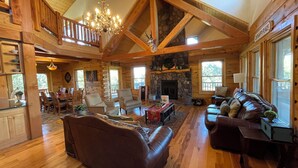 A spacious log cabin interior with a dining area, a fireplace, and a cozy living room with leather furniture. - Sugar Knoll Lodge / 3 Story, 5bdr, HOT TUB, East Zion, Bryce and Grand Canyon  (Orderville)