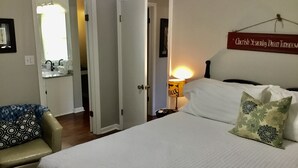 A bedroom with a bed, a bedside lamp, a chair, and a wall sign.