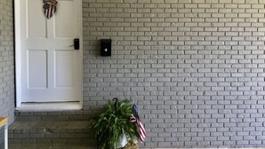 A white door with a welcome sign, a brick wall, a mailbox, and a potted plant with an American flag.