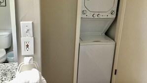 A compact laundry room with a washing machine and dryer, a power outlet, and a towel dispenser.