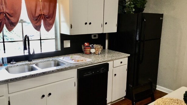 A kitchen with white cabinets, a black refrigerator, a dishwasher, and a window with curtains.