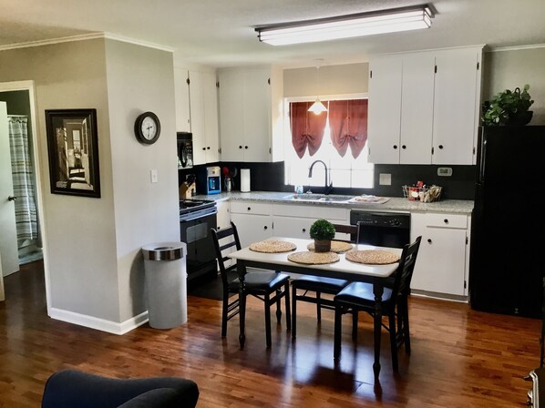 Una cocina moderna con armarios blancos, un refrigerador negro y un comedor con mesa y sillas.