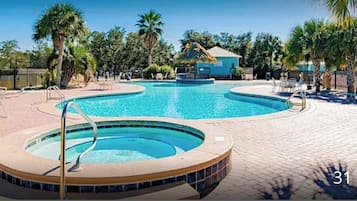 A swimming pool with a hot tub, surrounded by lounge chairs and palm trees.