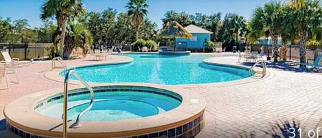 A swimming pool with a hot tub, surrounded by lounge chairs and palm trees.
