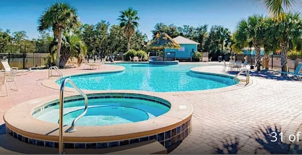 A swimming pool with a hot tub, surrounded by lounge chairs and palm trees.