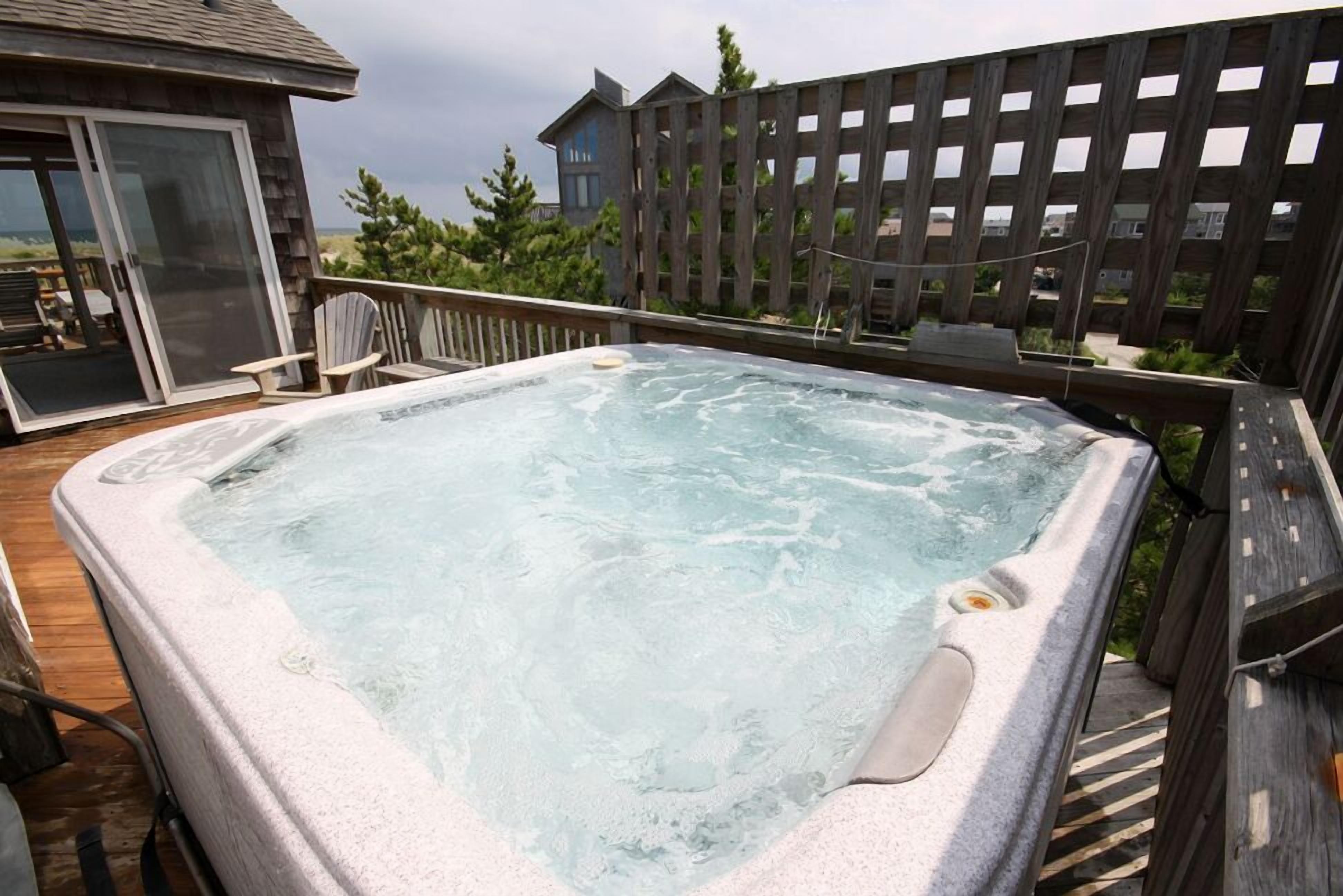 Un jacuzzi en una terraza de madera con vista a una casa y árboles al fondo.