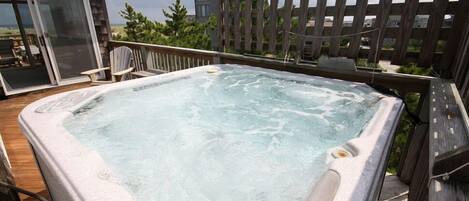 Un jacuzzi en una terraza de madera con vista a una casa y árboles al fondo.