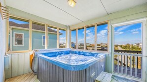 Una vasca idromassaggio su un pontile di legno con ampie finestre che si affacciano su una zona residenziale.