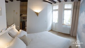Een slaapkamer met een groot bed, een kledingkast, een spiegel en een wandlamp.