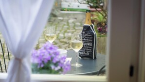 Een tafel met een fles wijn en twee glaasjes, een krijtbordmenu en uitzicht op een tuin door een raam.