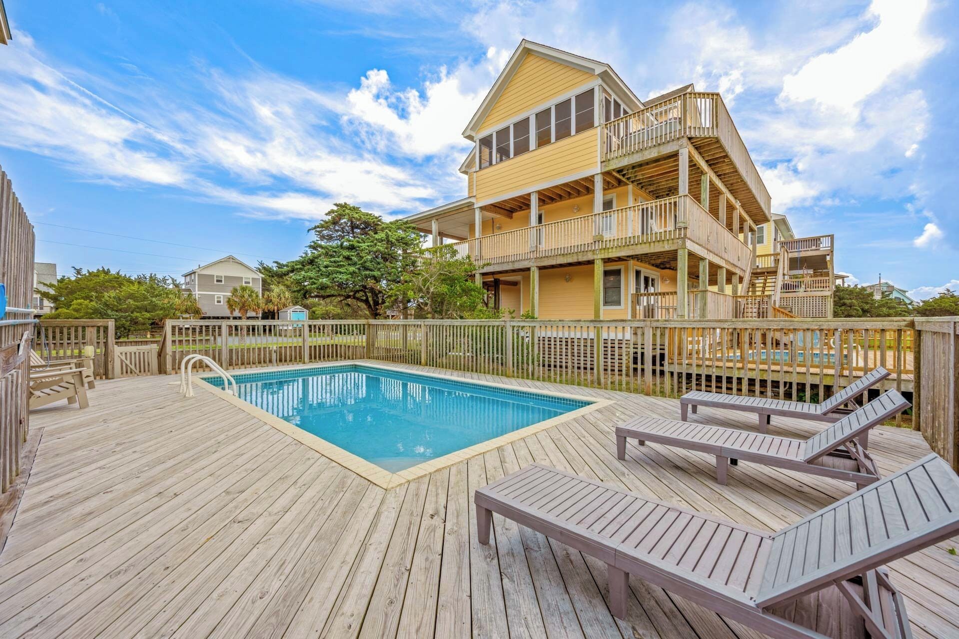 A two-story building with a pool and deck chairs.