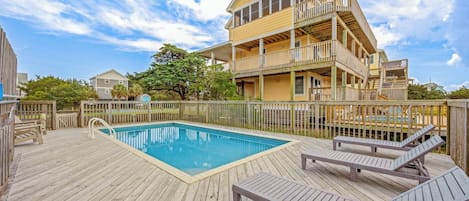 Un edificio de dos pisos con piscina y sillas de deck.