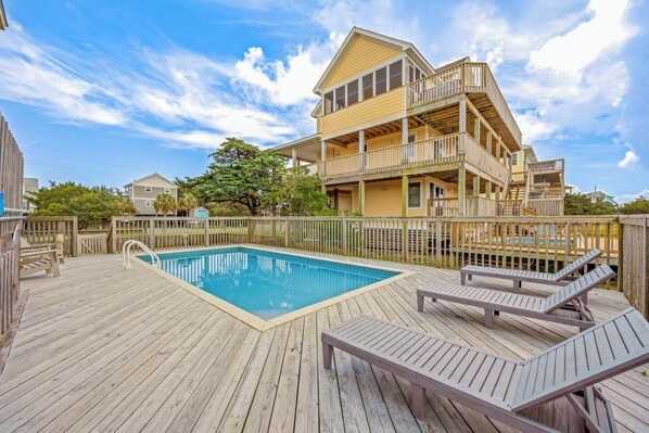A two-story building with a pool and deck chairs.