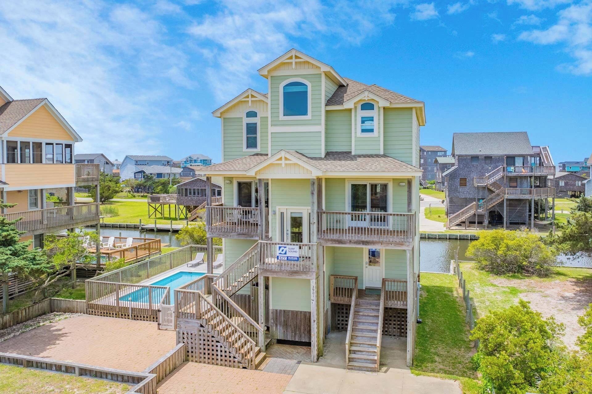 A multi-story residential building with a pool, wooden deck, and a sign indicating a surf sound.