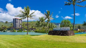 Un panneau indiquant « Hawaii Kai », avec en arrière-plan un lac, des palmiers et un bâtiment.