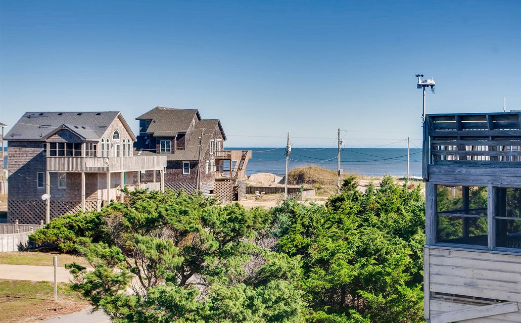 A coastal residential area with houses and a wooden structure, likely a beach house, with a view of the ocean.