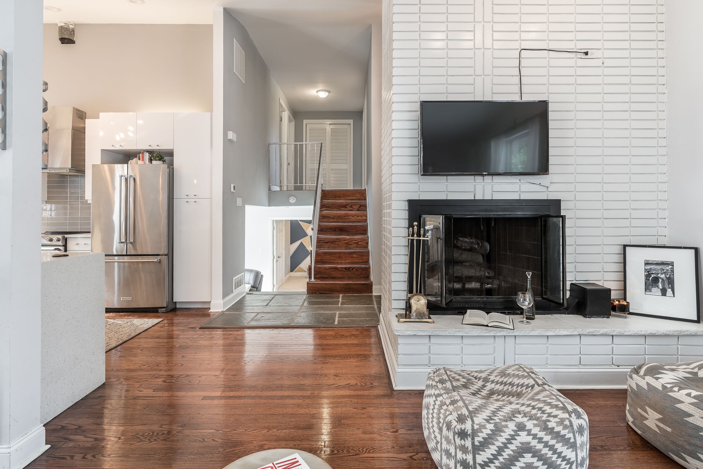 A modern living room with a fireplace, a flat-screen TV mounted above it, and a staircase leading to an upper level.