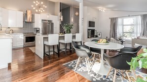 A modern kitchen with white cabinets, a stainless steel refrigerator, and a dining area with a round table and chairs. - Newly Renovated Mid-Century Home (Newtown Square)