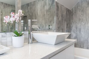 Un baño moderno con un lavamanos blanco, grifo cromado y una orquídea en maceta.