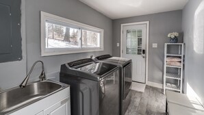 A laundry room with stainless steel appliances, a window, and a white door. - Newly Renovated Mid-Century Home (Newtown Square)