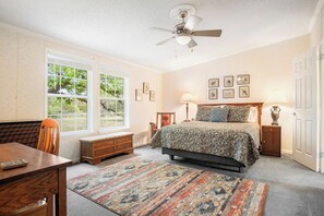 Een slaapkamer met een bed, nachtkastjes, een bureau, een stoel, een raam en een plafondventilator.
