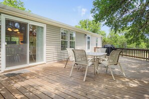 Un patio techado con una mesa y sillas, una puerta corrediza de vidrio y vista a un jardín trasero.