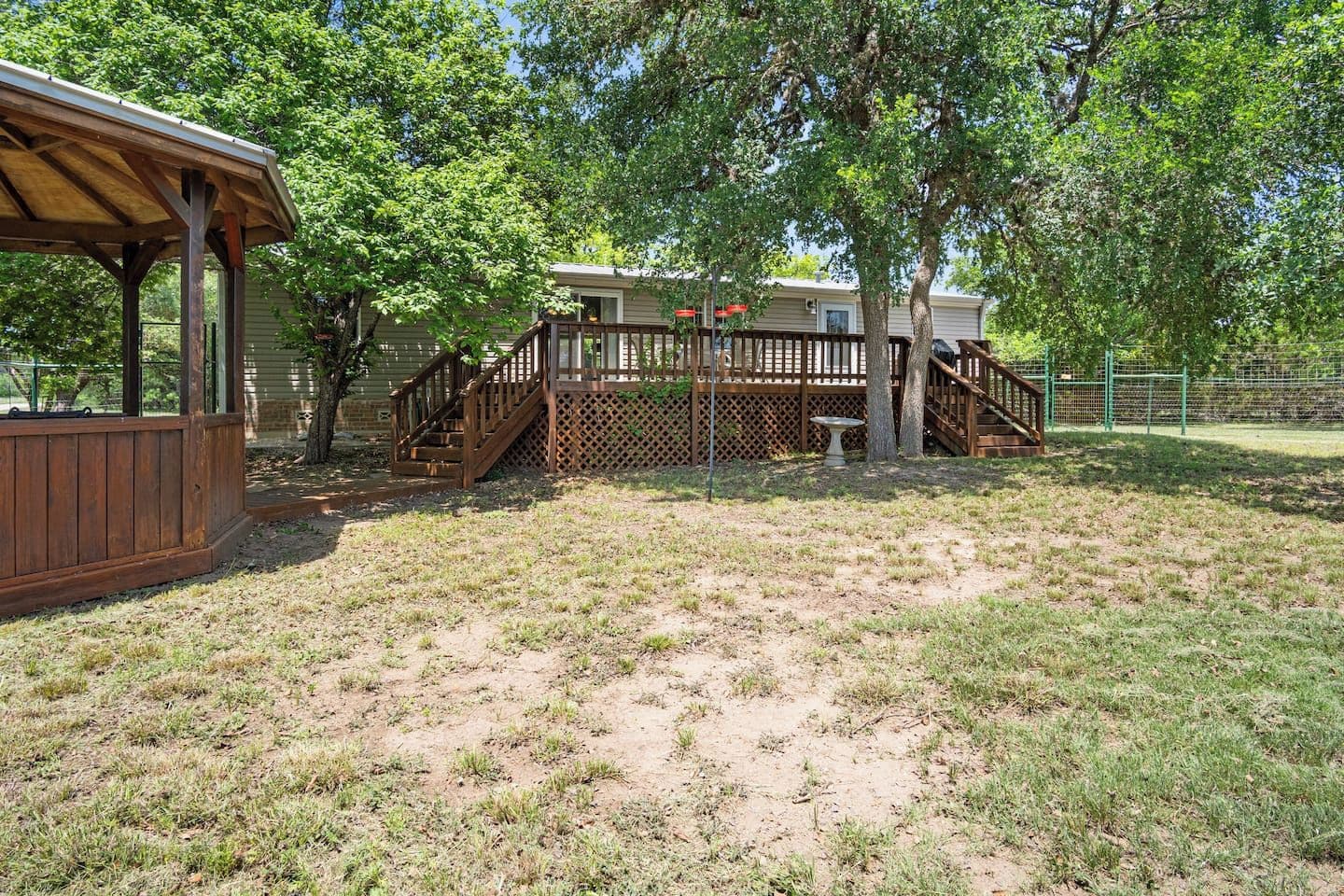 A wooden deck with a staircase leading to a covered area, surrounded by trees and a fenced yard.