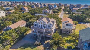 Uma área residencial costeira com casas, incluindo uma casa de dois andares com varanda e escadas que levam a um deck, e vista para o oceano.